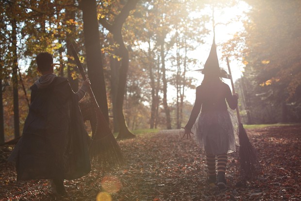 Siblings dressed up as witch and wizard for halloween, walking in the park.